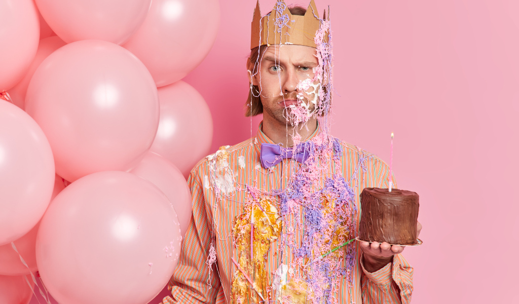 Мужчина принц с тортом и шариками на розовом фоне
