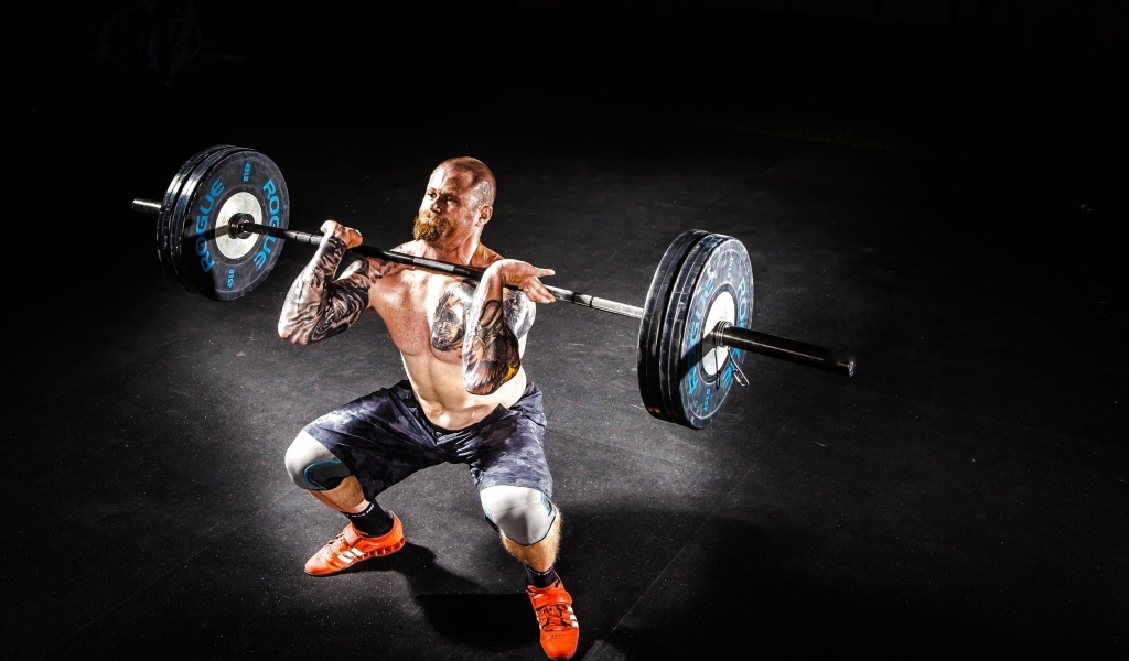 Сильный мужчина с татуировками на теле поднимает штангу