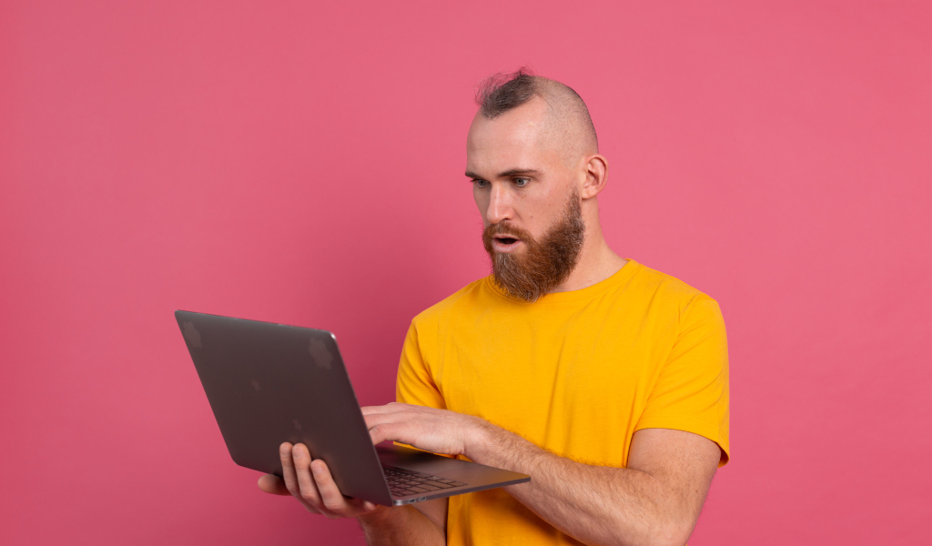 Удивленный мужчина с ноутбуком на розовом фоне