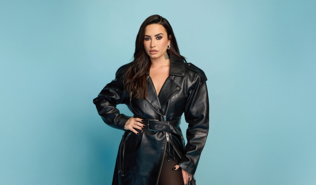 Певица Деми Ловато в кожаном черном пальто на голубом фоне