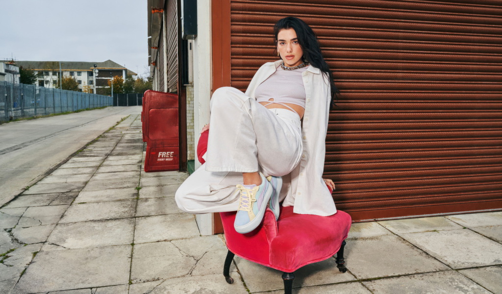 Певица Дуа Липа в белом костюме на кресле у стены