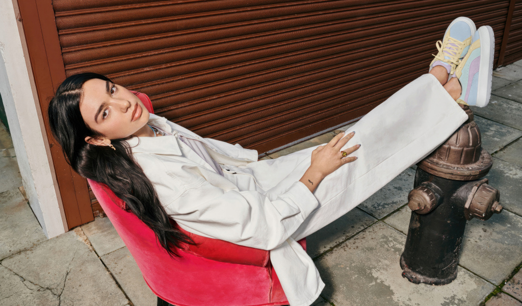 Певица Дуа Липа в белом костюме сидит в кресле