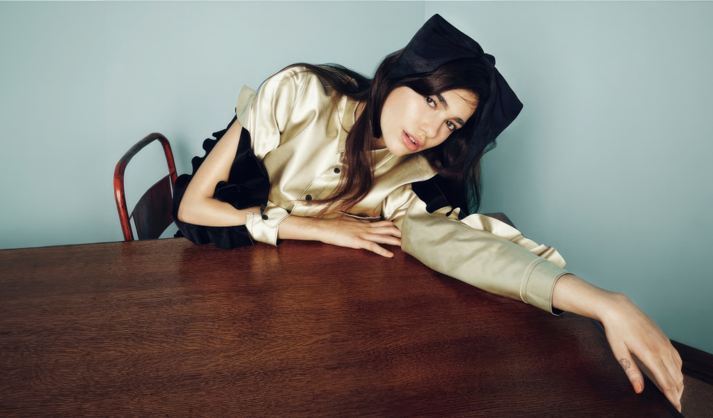 Певица Дуа Липа сидит за деревянным столом