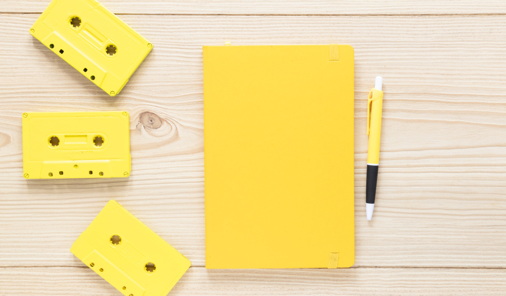 Желтый блокнот с ручкой и кассетами на столе