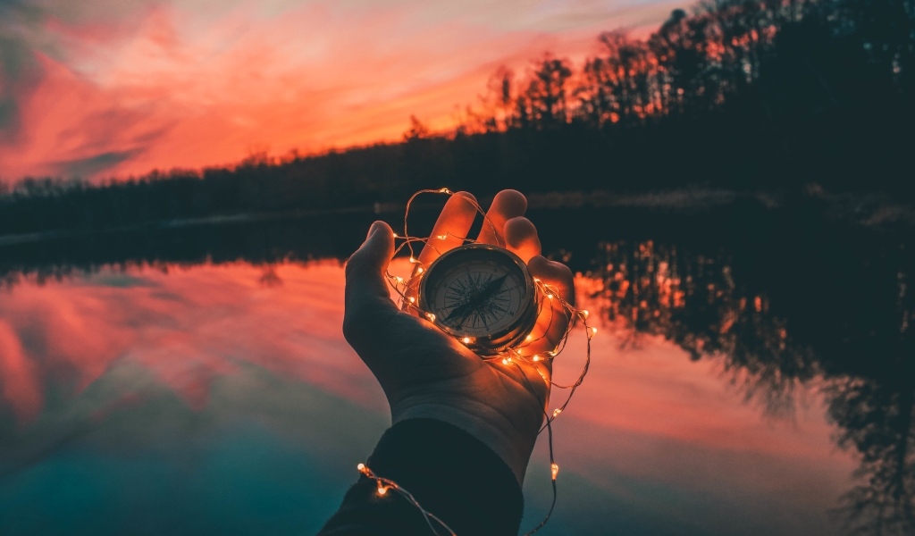 Компас с гирляндой в руке у реки