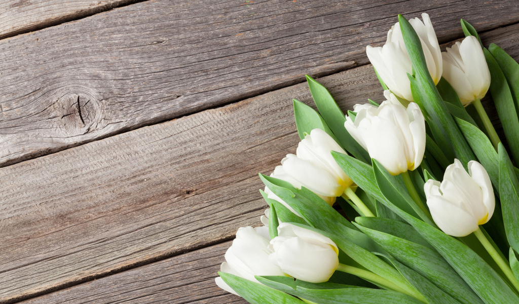 Букет нежных белых тюльпанов с зелеными листьями на деревянном столе