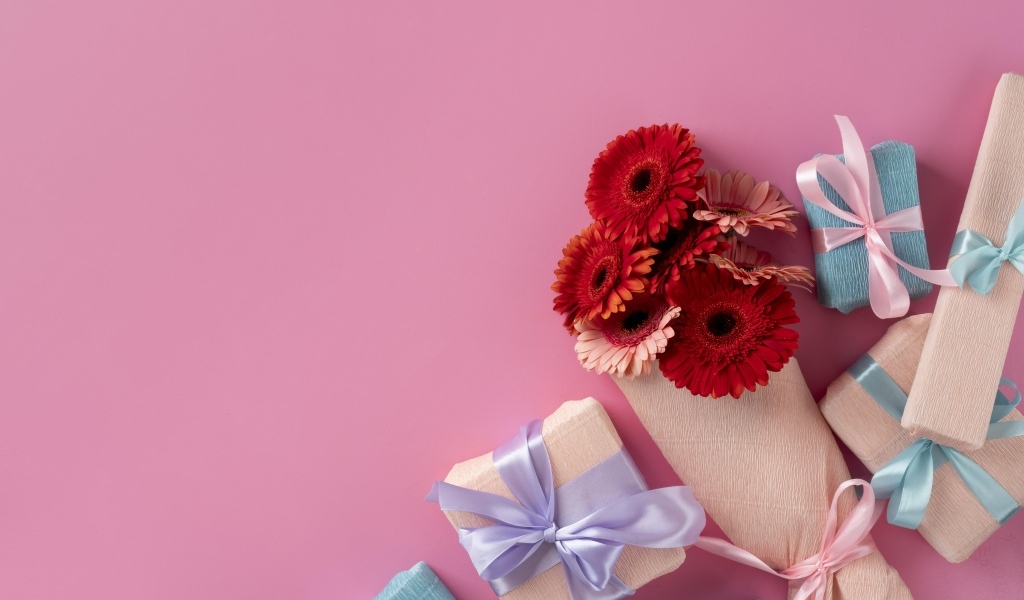Букет цветов герберы с подарками на розовом фоне