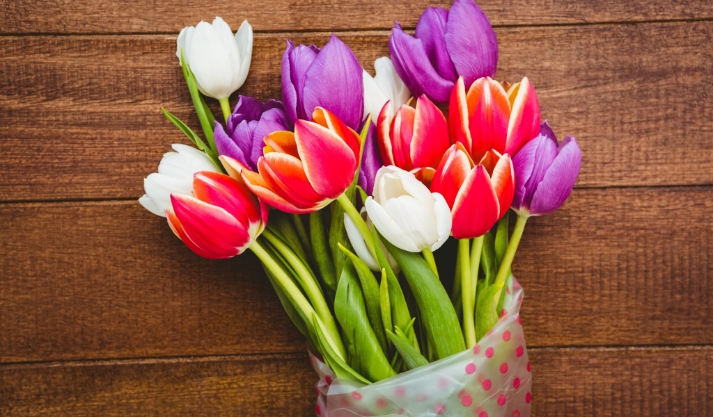 Букет разноцветных тюльпанов в пакете на деревянном фоне