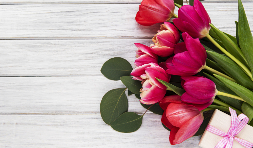 Букет розовых тюльпанов с подарком и зелеными листьями на белом столе