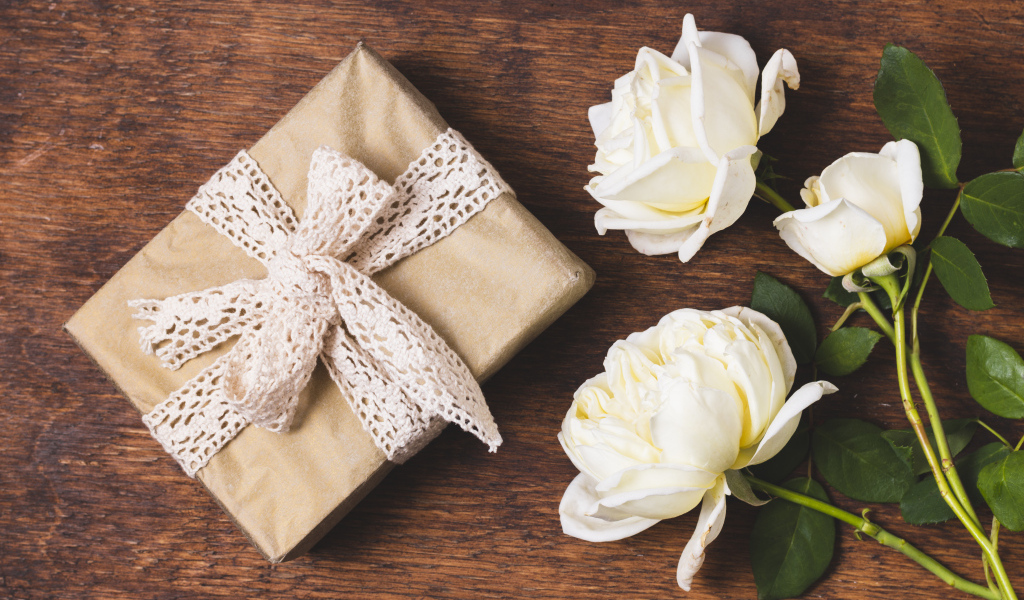 Коробка с подарком на деревянном столе с белыми розами