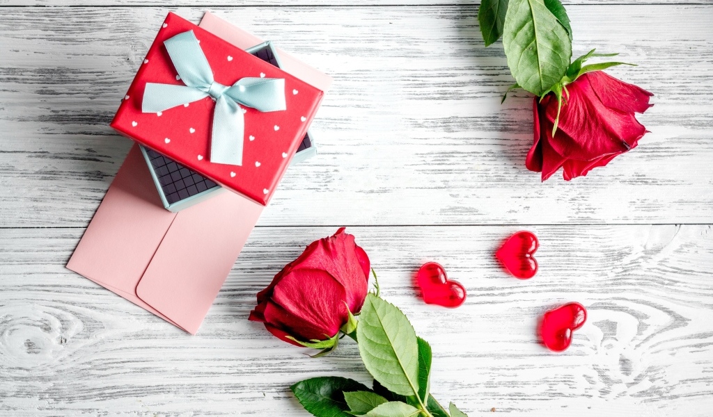 Две красные розы с подарком и сердечками на столе