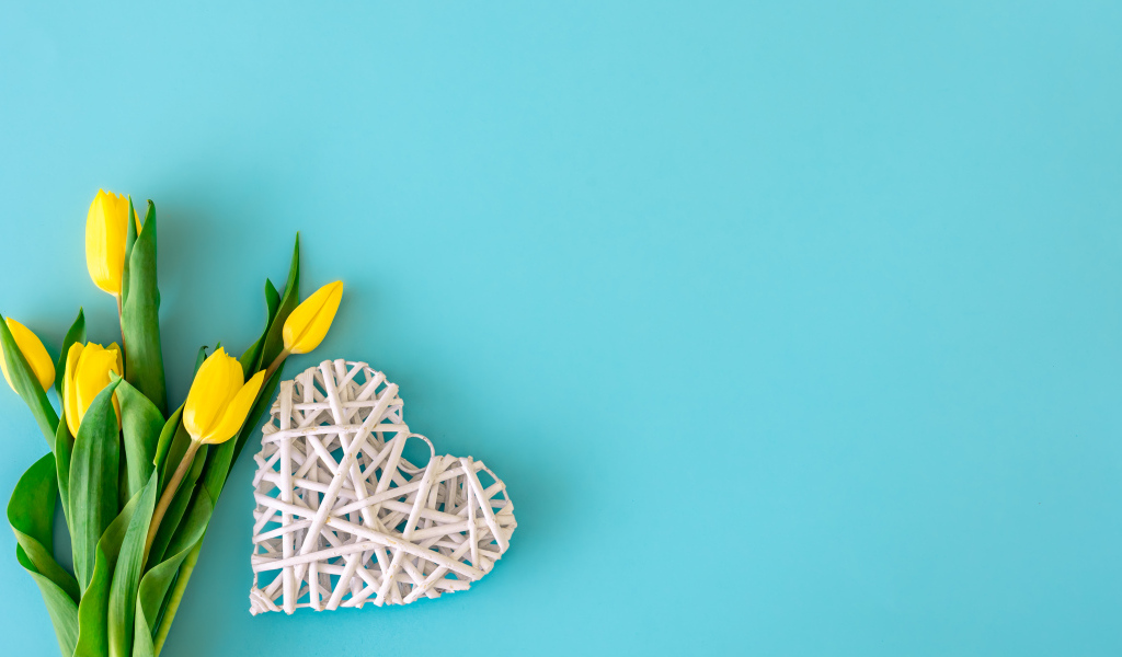 Белое плетеное сердце с букетом желтых тюльпанов на голубом фоне