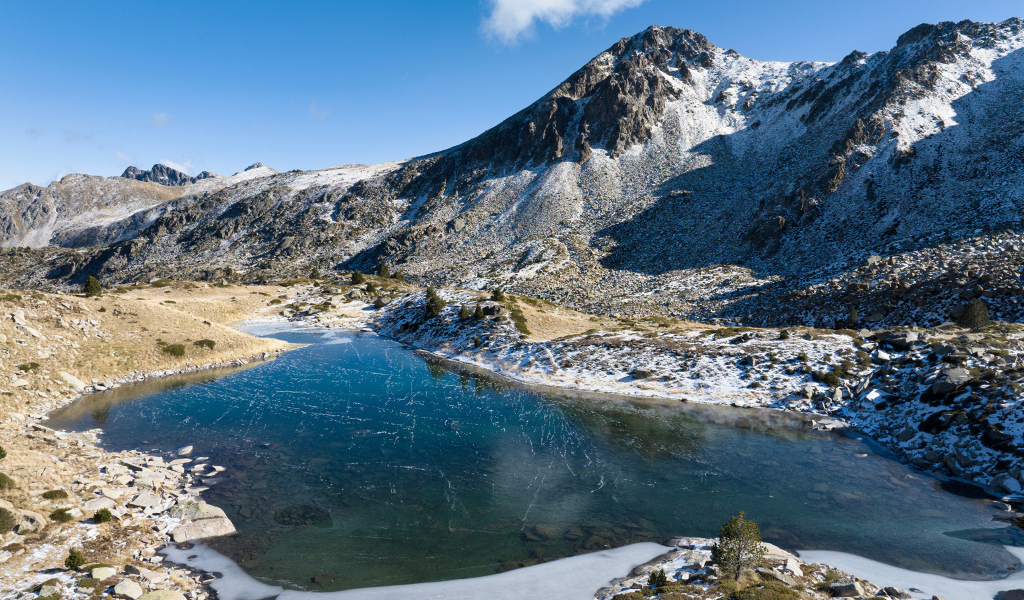 Покрытое льдом озеро в заснеженных горах в лучах солнца, Андорра
