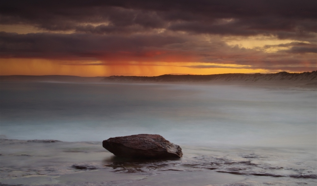 Большой камень в воде на фоне грозового неба в море