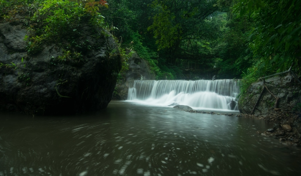 Водопад стекает в реку с большими камнями в лесу