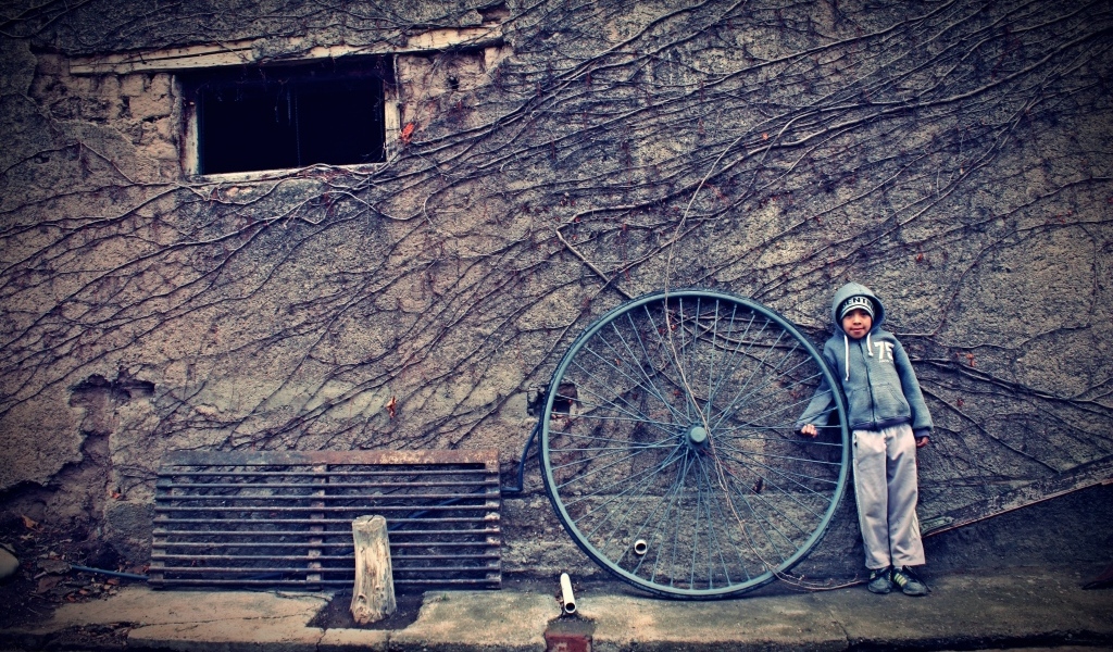 Мальчик с большим колесом стоит у стены