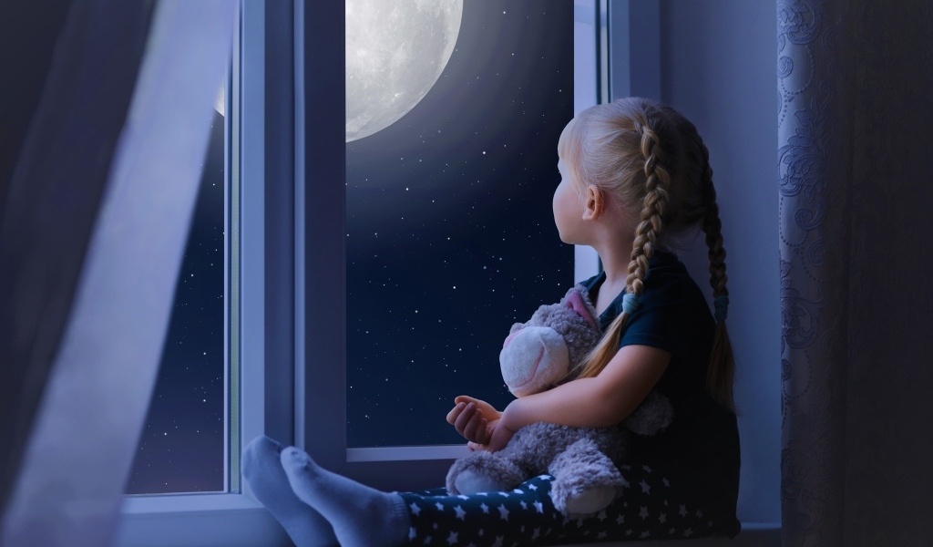 Маленькая девочка с игрушкой смотрит у окна на луну