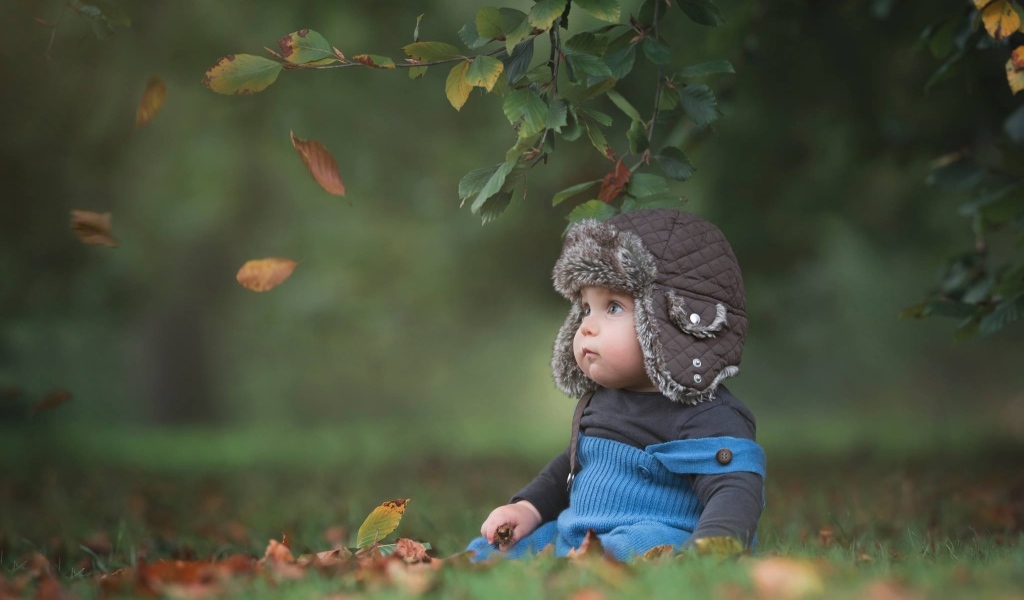 Карапуз в шапке сидит под деревом осенью