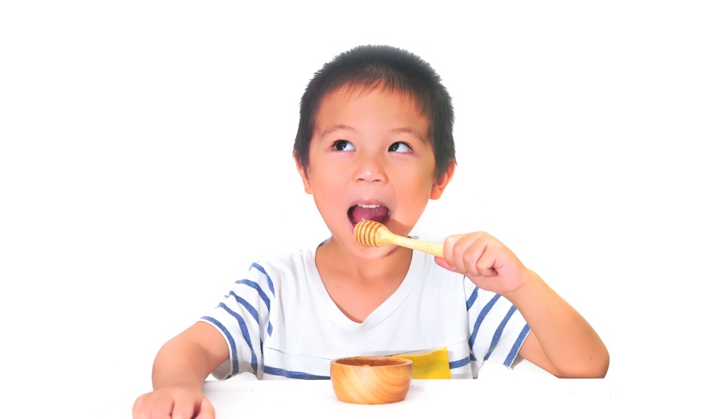 Мальчик азиат ест мед на сером фоне