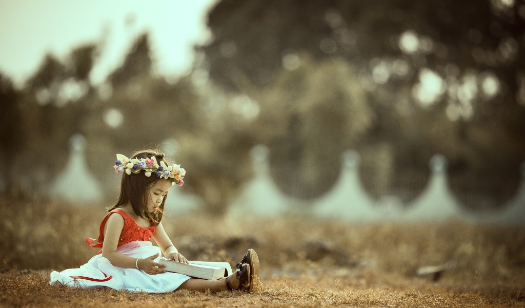 Девочка азиатка сидит с книгой на земле