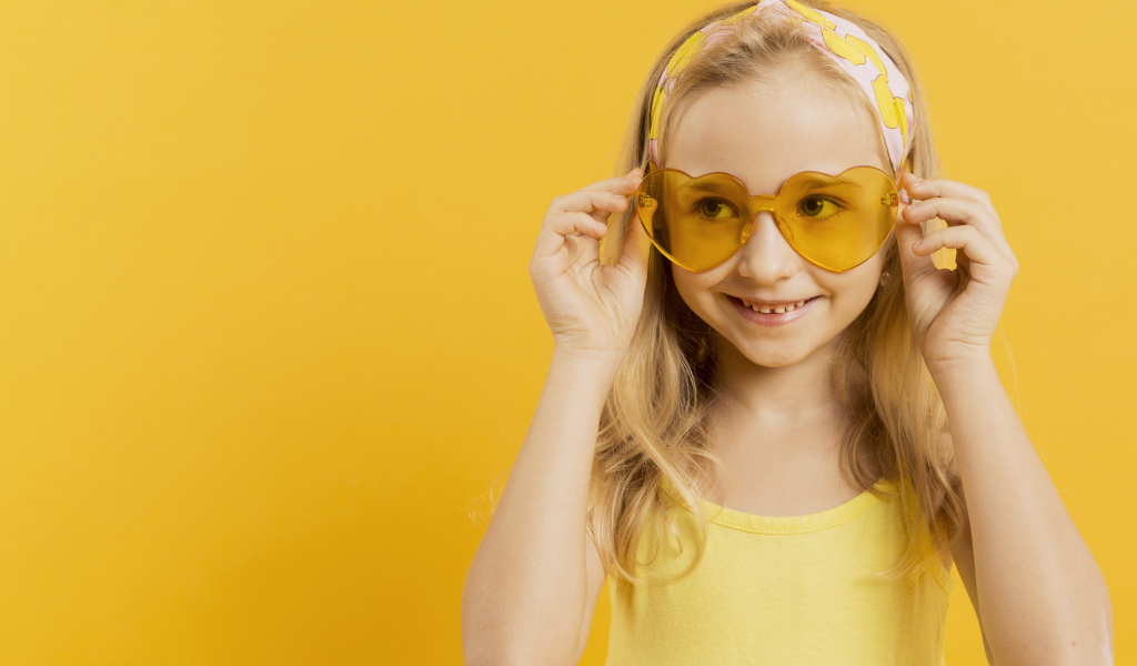 Красивая девочка блондинка в очках в форме сердца на желтом фоне