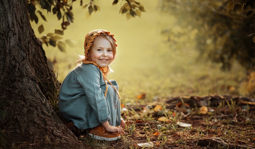 Красивая улыбающаяся девочка сидит под деревом