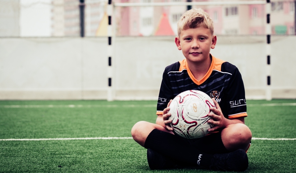 Мальчик футболист сидит на траве с мячом