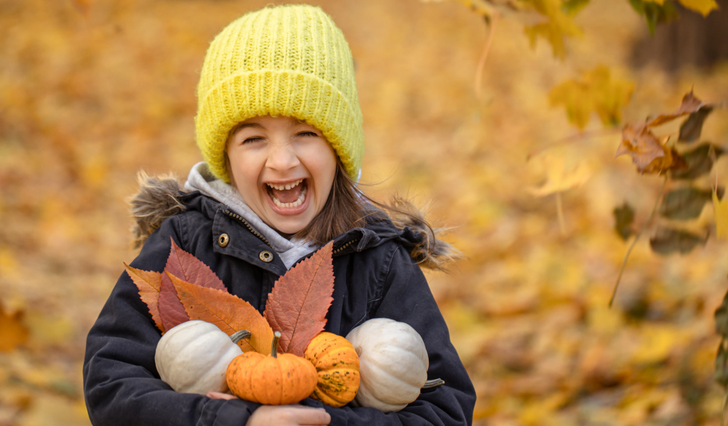 Веселая девочка с тыквами и листьями в руках осенью