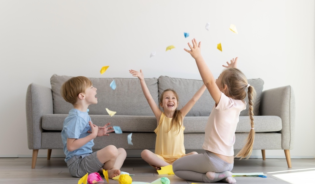 Дети играют на полу  в комнате с серым диваном