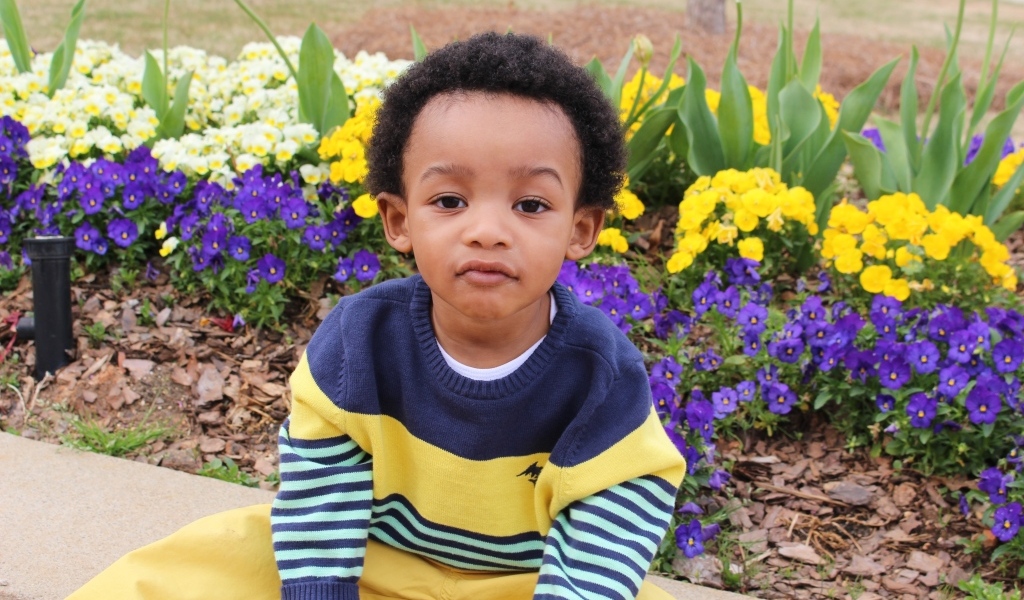 Темнокожий мальчик у клумбы с цветами 