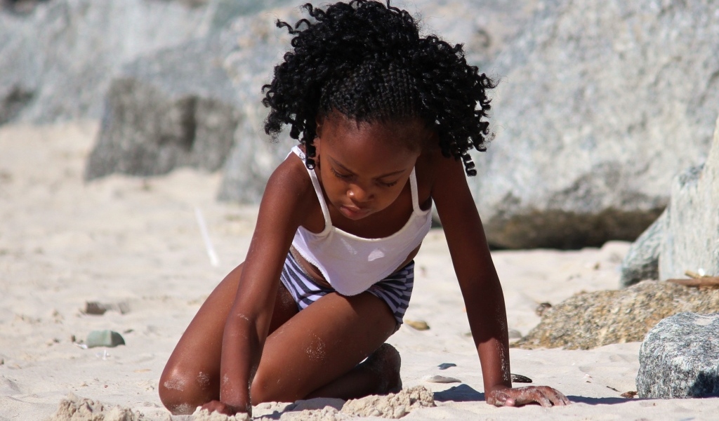 Темнокожая маленькая девочка играет на песке на пляже