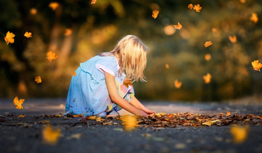 Девочка в платье играет с листьями на дороге