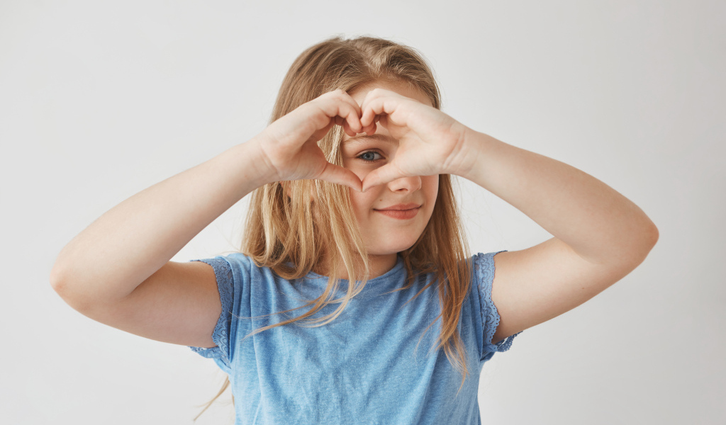 Девочка делает сердечко руками на сером фоне