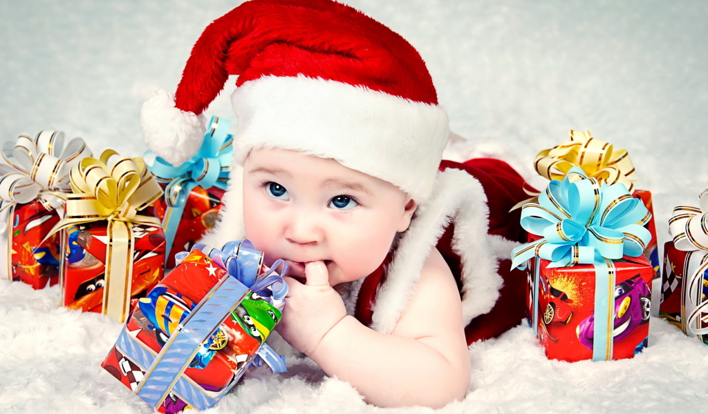 Грудной ребенок в новогодней шапке с подарками на покрывале