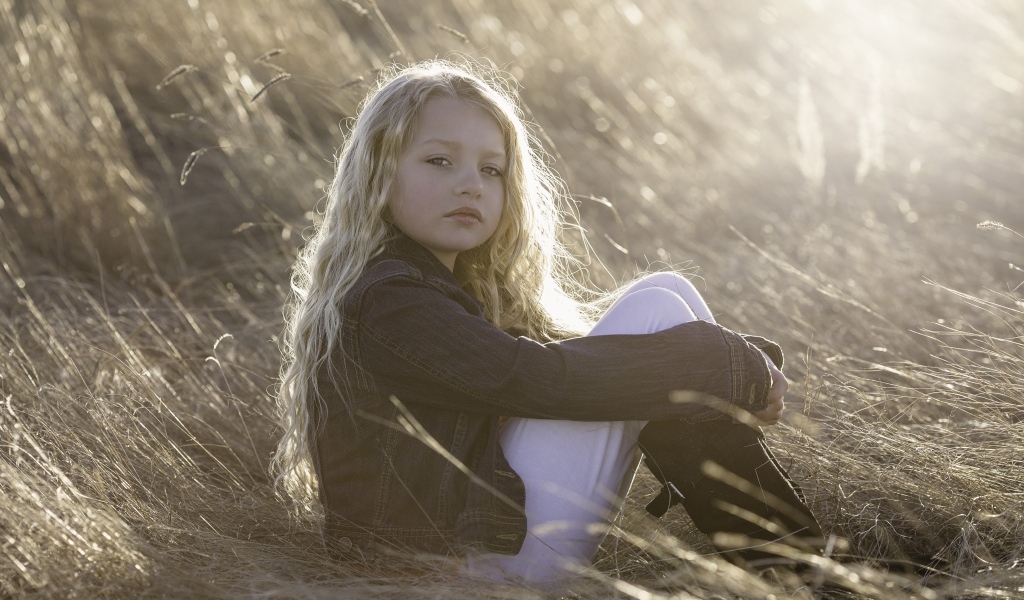 Маленькая светловолосая девочка сидит на сене