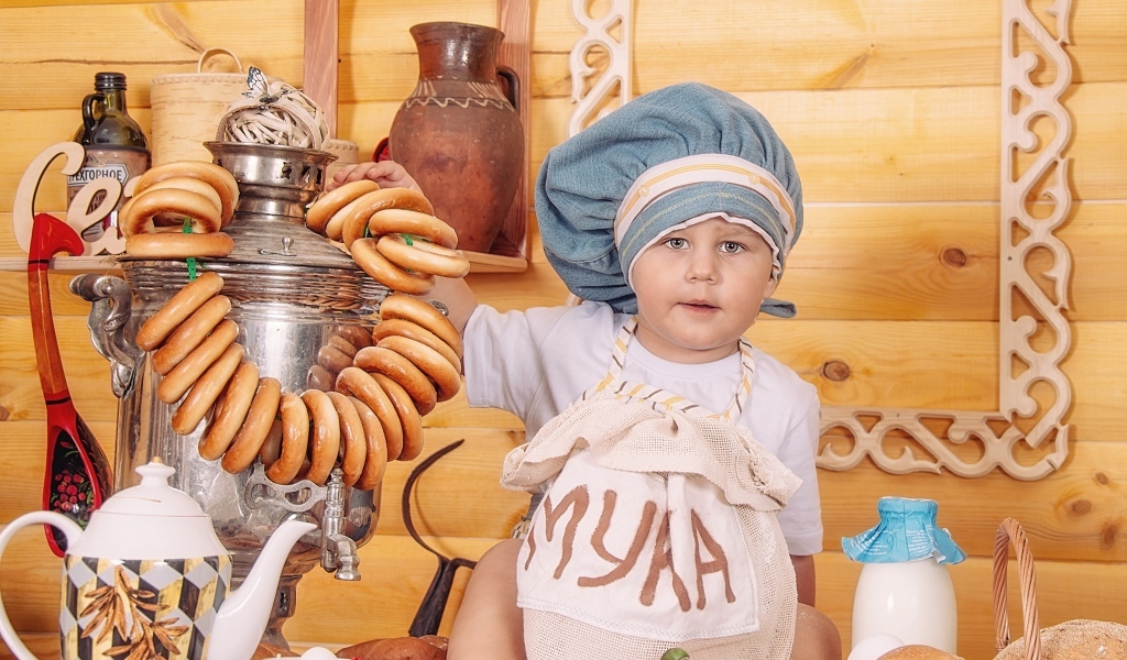 Маленький мальчик повар с продуктами и самоваром на столе