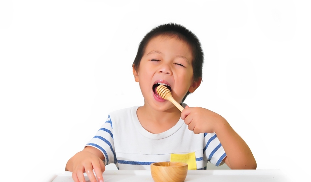Маленький мальчик ест мед на белом фоне
