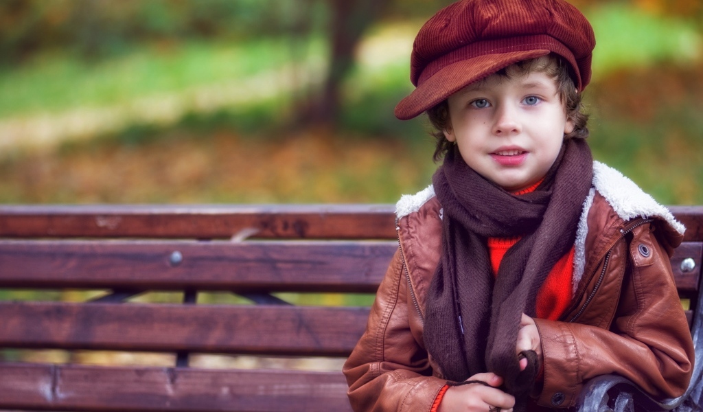 Маленький мальчик в куртке на лавке в парке осенью