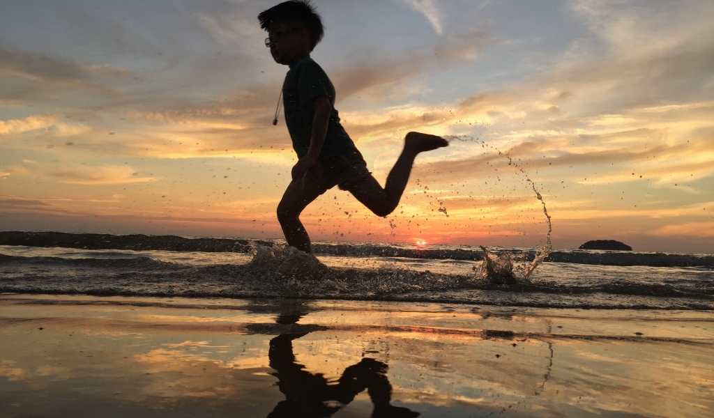 Маленький мальчик бежит по воде на закате