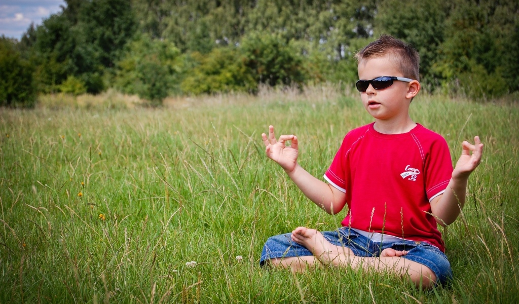 Маленький мальчик в очках медитирует на зеленой траве