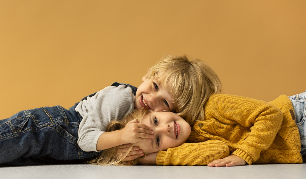 Маленькие брат и сестра лежат на полу на желтом фоне