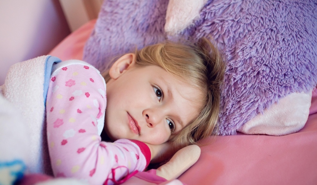 Маленькая кареглазая девочка лежит в кровати 