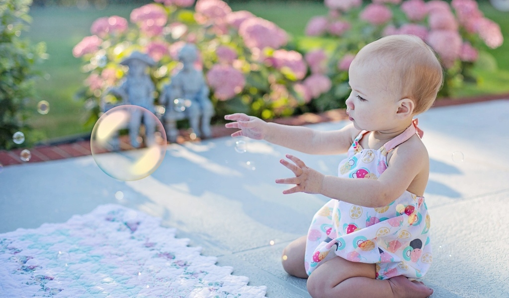 Маленькая девочка ловит мыльный пузырь