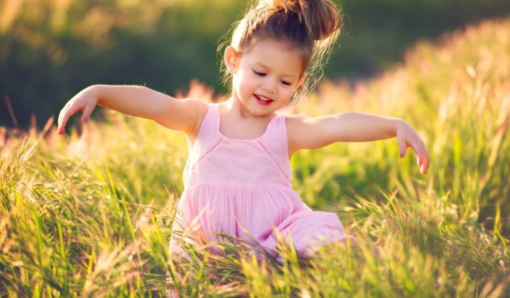 Маленькая девочка в розовом платье в зеленой траве