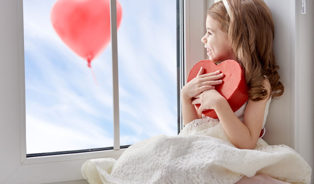 Маленькая девочка с коробкой в форме сердца сидит у окна