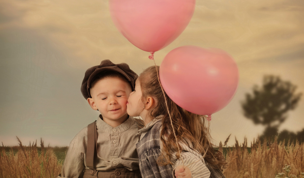 Маленькая девочка с шариками целует мальчика