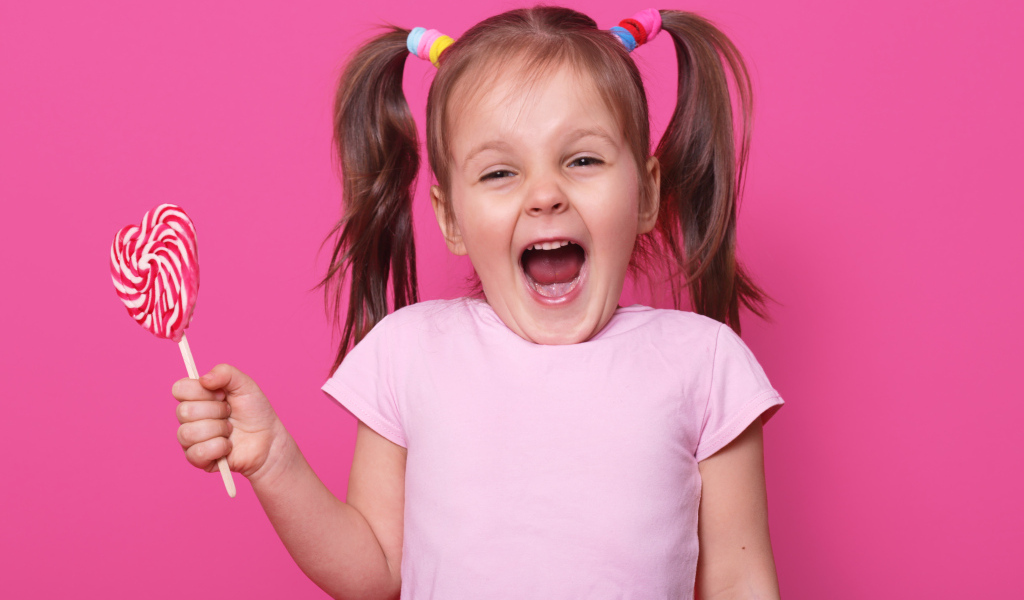 Маленькая девочка с леденцом на розовом фоне