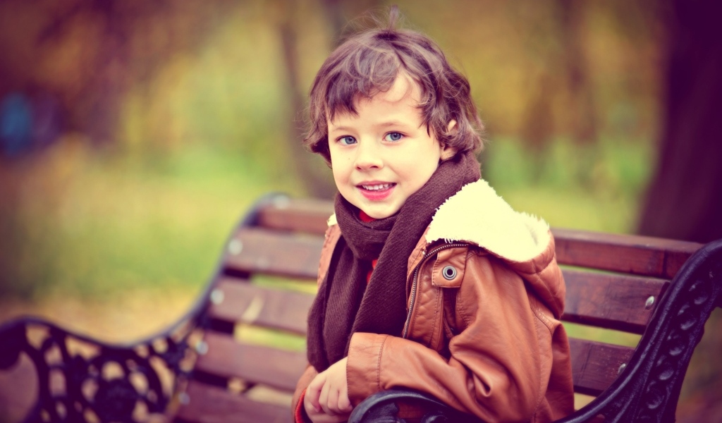 Маленький улыбающийся мальчик на лавке в парке
