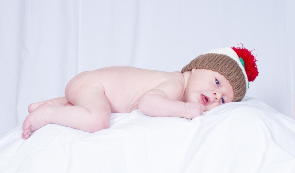 Новорожденный малыш в шапке на белой подушке