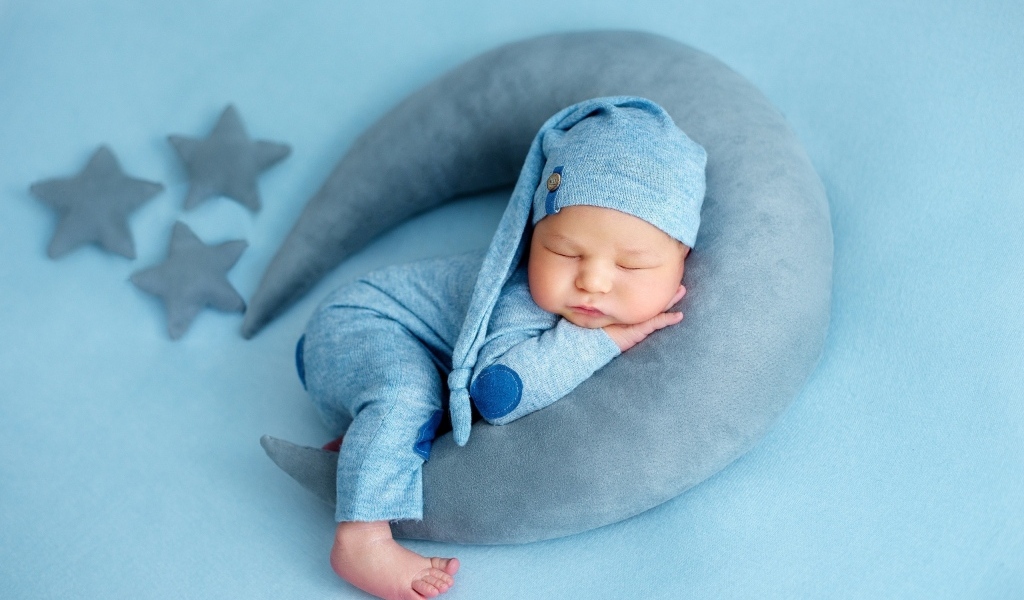 Новорожденный малыш спит на игрушечном полумесяце на голубом фоне